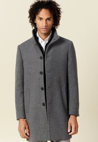 Abrigo de lana gris con un cuello estructurado, seis botones negros y bolsillos laterales. La tela parece suave con un acabado ligeramente texturizado.