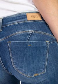 Jeans in denim blu con un classico design a cinque tasche e una toppa in pelle sulla vita posteriore, che dettaglia il nome e il logo del marchio.