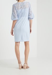 Krótka niebieska sukienka z koronkowym topem i bufkami, charakteryzująca się gładką fakturą materiału i zapięciem z tyłu. Uzupełniona beżowymi sandałkami na paski.