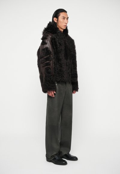 Melna aitu āda ar brūnām ādas piedurknēm, ar faktūru. Saskaņots ar tumši zaļiem biksēm un melnām kurpēm.