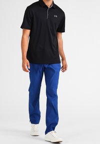 Czarny polo z kołnierzykiem i szarymi akcentami, w połączeniu z niebieskimi spodniami i białymi tenisówkami. Prosty i funkcjonalny design.