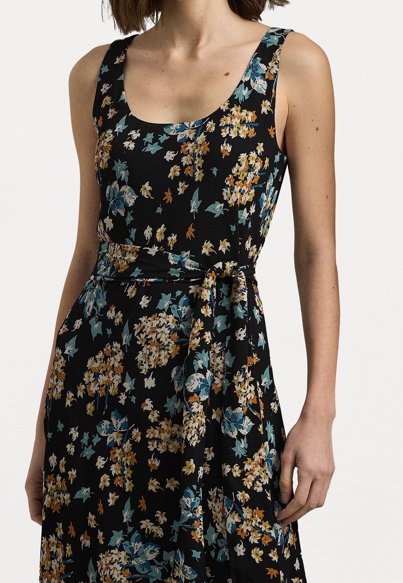 Ärmlös svart klänning med blå, orange och vit blommönster, med en rundad halsringning och ett knytbälte i midjan.