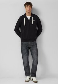 Czarny pulower z półzamek, białymi sznureczkami i wyhaftowanym logo, połączony z ciemnymi dżinsami i białymi trampkami.