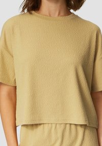 Helles beige Kurzarmoberteil mit einem strukturierten Wellenmuster, rundem Ausschnitt und lockerer Passform, ergänzt durch ein passendes Unterteil.