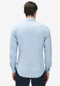Ljusblå långärmad skjorta med knäppning vid ärmsluten och rundad nederkant. Tillverkad av strukturerad tyg, med en bakåtkant och en ren design.