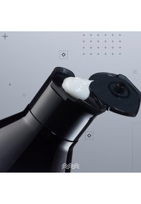 Svart plastflaska med en spetsig flip-top lock, som dispenserar en vit krämig substans. Slät textur med en elegant design. Minimalistisk bakgrund.