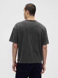 Γκρι κοντομάνικο μπλουζάκι από βαμβάκι με χαλαρή εφαρμογή. Ακατέργαστο τελείωμα και στρογγυλή λαιμόκοψη, με απαλή, ελαφρώς υφασμένη υφή.