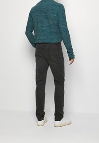Tmavě šedé kalhoty s slim fit designem, které mají pět kapes a klasický pas. V kombinaci s dlouhým rukávem ve struktuře v barvě smaragdově zelené a bílými teniskami.
