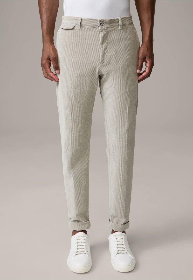 Pantalon en velours côtelé beige clair à coupe droite, poches avant, fermeture par boutons, revers roulés, associé à des baskets blanches. Texture lisse.