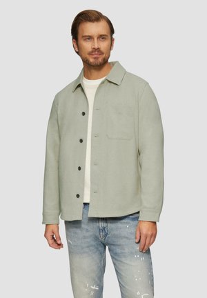 Lichtgroene button-up jas met een enkele borstzak, gemaakt van zachte stof, gecombineerd met lichtblauwe versleten jeans.