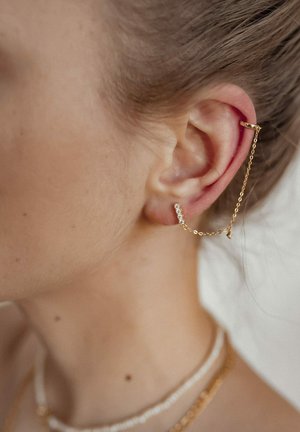 Goldener Ohr-Cuff mit einer Kette, die mit einem kristallbesetzten Stab verbunden ist. Eng anliegendes Design, glatte Textur, minimalistische Details, hinter dem Ohr befestigt.