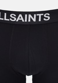 Boxers noirs avec une large ceinture noire portant le texte "ALLSAINTS" en blanc. Tissu lisse avec des détails de couture subtils.