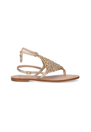 Sandalia plana dorada con adornos de joyas, con un diseño de tira T, correa ajustable en el tobillo y una suela plana marrón.