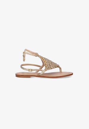 Sandalia plana dorada con adornos de joyas, con un diseño de tira T, correa ajustable en el tobillo y una suela plana marrón.