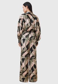 Blusa di seta e pantaloni a gamba larga con uno sfondo nero e un motivo colorato di foglie e fiori. Vestibilità morbida con vita elasticizzata.