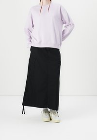 Lichtpaarse trui met lange mouwen, gecombineerd met een lange zwarte rok met cargozakken en witte sneakers. Eenvoudig, modern ontwerp.