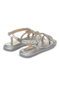 Silberne flache Sandalen mit dekorativen klaren Edelsteinen, die überkreuzte Riemen und eine strukturierte metallische Oberfläche an der Sohle aufweisen.