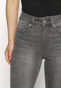 Jeans de ganga cinza com um design ajustado, disposição padrão de cinco bolsos e fecho de botão com um discreto detalhe de desgaste.