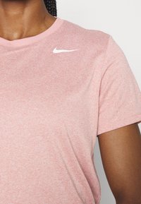 Camiseta de algodón melange rosa con mangas cortas, escote redondo y un logo de Nike en blanco en la parte superior izquierda. Textura suave y ajuste casual.