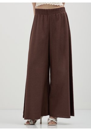 Pantalon marron à jambes larges avec taille élastique porté avec des sandales blanches à talons et un top court en dentelle blanche.