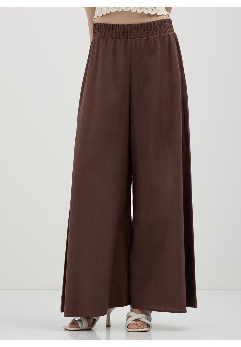 Pantalon marron à jambes larges avec taille élastique porté avec des sandales blanches à talons et un top court en dentelle blanche.