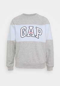Grå sweatshirt med ljusblå horisontell rand och "GAP Original"-logotyp i fet marinblå och röd text. Mjuk textur, rund halsringning och ribbade ärmslut.