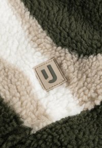 Textúrovaný fleece materi�ál s zelenými, krémovými a béžovými chevron vzormi, so štvorcovou nášivkou s elegantným „J.“