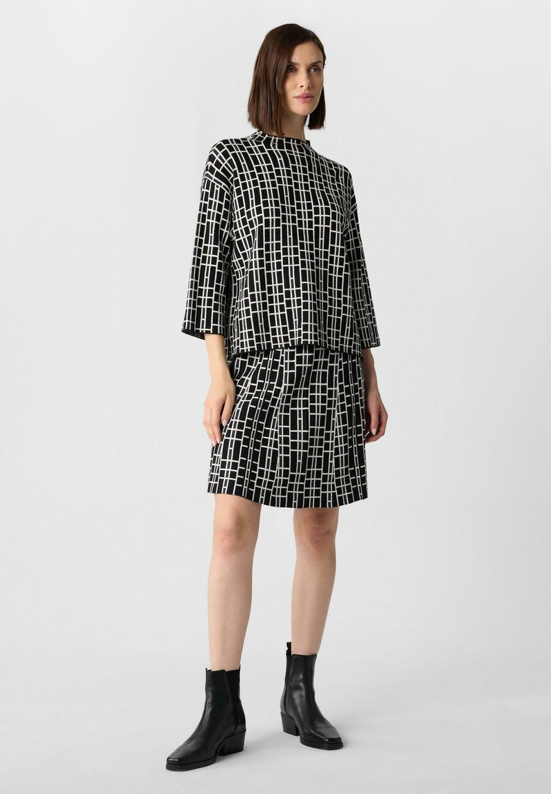 Top a righe bianco e nero con maniche a tre quarti abbinato a una gonna coordinata, caratterizzata da un design geometrico e una texture particolare.