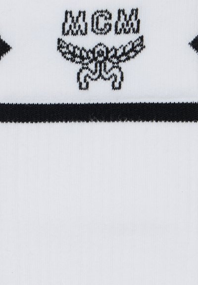 Λευκές κάλτσες με μαύρη οριζόντια ρίγα που φέρει τα γράμματα "MCM" και ένα γραφικό αετού. Κατασκευασμένες από μαλακό, υφασμάτινο υλικό.