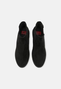 Bottes de cheville en suède noir avec des panneaux latéraux en élasthanne, un design épuré et un tissu texturé. Comprend une étiquette logo rouge à l'intérieur.