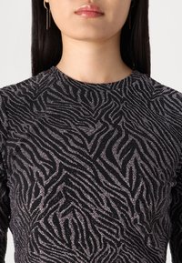 Mustapaita pitkähihaisilla hihoilla, jossa on hopeinen kimalteleva seeprakuosi. Pyöreä kaula-aukko ja sileä tekstuuri. Lähikuva kaula-aukosta ja ylärinta-alueesta.