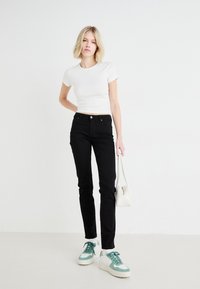 Sorte slim-fit jeans med en glat tekstur, parret med en hvid kortærmet top og sneakers med grønne accenter. En hvid håndtaske fuldender outfittet.