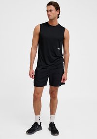 Zwarte mouwloze sportshirt met een ronde halslijn, gecombineerd met bijpassende zwarte shorts en zwarte sneakers. Eenvoudig ontwerp, zacht materiaal.