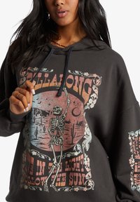 Sudadera negra con un diseño gráfico en el frente que presenta un esqueleto, una escena desértica y el texto "Vive en la Luz, Sigue al Sol." Tejido suave.