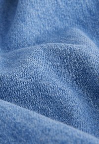 Gros plan d’un tissu denim bleu doux montrant la texture détaillée du tissage et des plis légers.