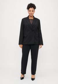 Μαύρο σακάκι διπλής όψης με λείο ύφασμα, με μεγάλα κουμπιά και αντίστοιχο κομμένο παντελόνι. Φορεμένο με μαύρες μυτερές γόβες.