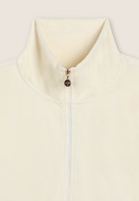 Giacca cremisi con zip e colletto alto, caratterizzata da una texture liscia e cuciture tonalità. Tirazip in metallo con dettaglio del logo.