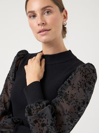 Black sweater with ribbed texture, featuring sheer puff sleeves adorned with black floral embroidery and a round neckline.