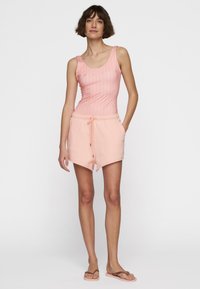 Top sin mangas de rayas en rosa claro con escote redondeado, combinado con unos pantalones cortos suaves en melocotón que cuentan con una cinturilla elástica y bolsillos frontales.