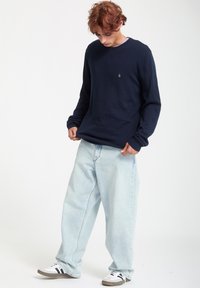 Marine crewneck sweater med lange ærmer, parret med lyseblå, vide bukser. Letvægtsmateriale, enkelt design og hvide sko med sorte striber.