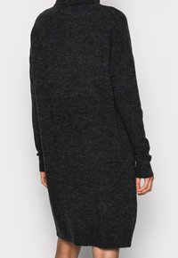 Överdimensionerad svart stickad klänning med hög krage, långa ärmar och en texturerad tyg. Längd till mitten av låret med ribbade avslut och kant.