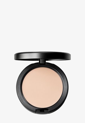 Boîte de maquillage compacte noire avec poudre pressée beige et couvercle ouvert sur un fond blanc uni.