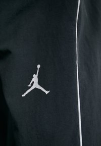 Black fabric with a white Jumpman logo. Features a clean design and a thin white stripe along the edge. Smooth texture.