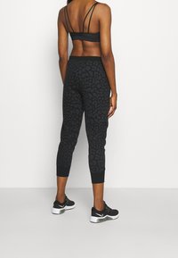 Leggings atléticos negros con estampado de leopardo texturizado, largo recortado y cintura elástica, combinados con un sujetador deportivo negro con tiras y zapatillas deportivas.