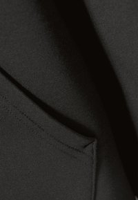 Gros plan sur un tissu noir lisse avec des coutures visibles formant un détail de couture triangulaire.