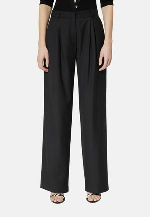 Kobieta ubrana w czarne szerokie spodnie zestawione z czarnym topem i sandałami na otwarte palce z czarnymi i białymi paskami.