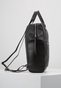 Zwarte leren rugzak met gouden rits, verstelbare schouderbanden en bovenhandvatten, zijwaarts weergegeven op een witte ondergrond.