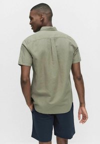 Korte mouwen, olijfgroene shirt gemaakt van lichtgewicht stof, met een rugnaaddetail en een klassieke kraag, gecombineerd met donkere shorts.