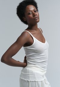 White camisole top made of lightweight fabric, featuring thin straps and a v-neck design, worn with a flowing white layered bottom.