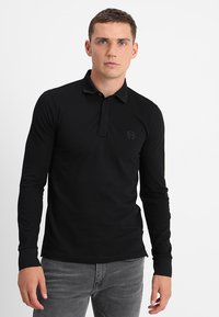 Polo a maniche lunghe nera con colletto e un logo discreto sul petto. Realizzato in un tessuto liscio e leggero.